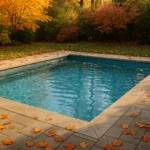 Piscina limpia de obra rodeada de hojas secas de otoño con árboles de colores cálidos al fondo.