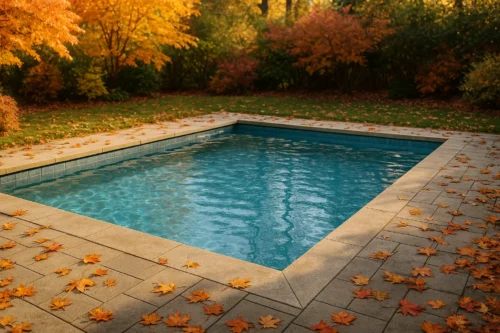 Piscina limpia de obra rodeada de hojas secas de otoño con árboles de colores cálidos al fondo.
