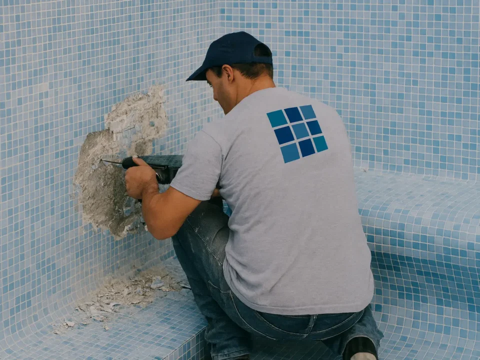 Operario con pistolete retirando gresite de la pared de una piscina vacía en proceso de reparación.